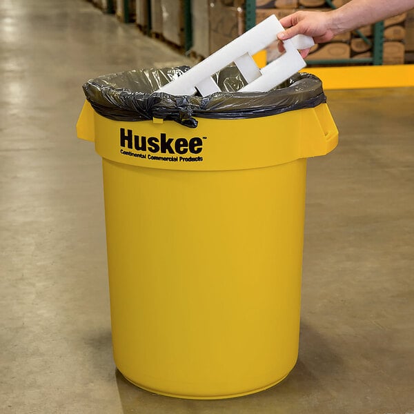 A person holding a yellow Continental 32 gallon trash can.