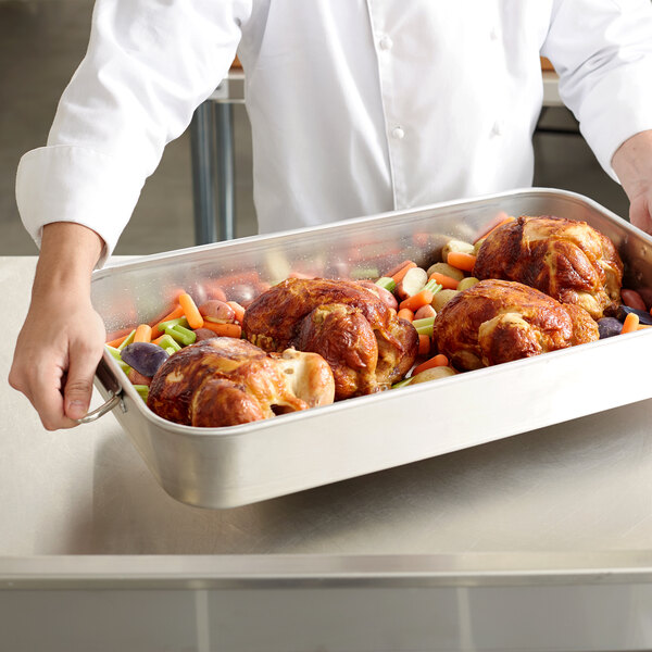 A chef holding a Vollrath Wear-Ever aluminum roasting pan with cooked turkey.