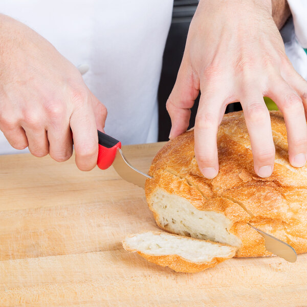 A person using a Mercer Culinary Millennia Colors bread knife to cut a piece of bread.