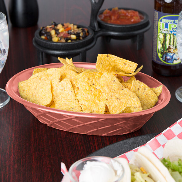 A paprika oval weave basket filled with chips on a table.