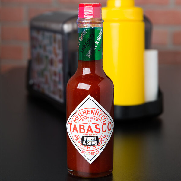 A yellow and green TABASCO® Sweet & Spicy Hot Sauce bottle on a table.