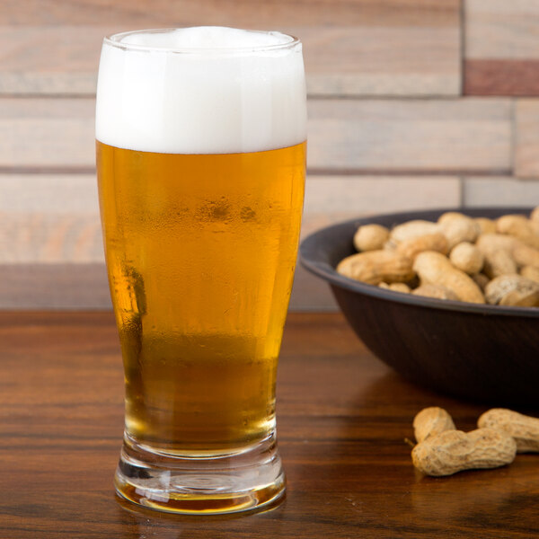 An Anchor Hocking Barbary pub glass of beer on a table with a bowl of peanuts.