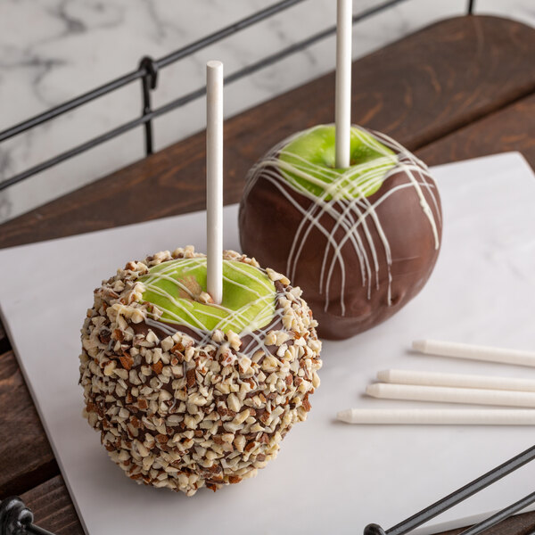 A chocolate covered green apple with nuts on a Paper Pointed Candy Apple Stick on a tray in a bakery display.