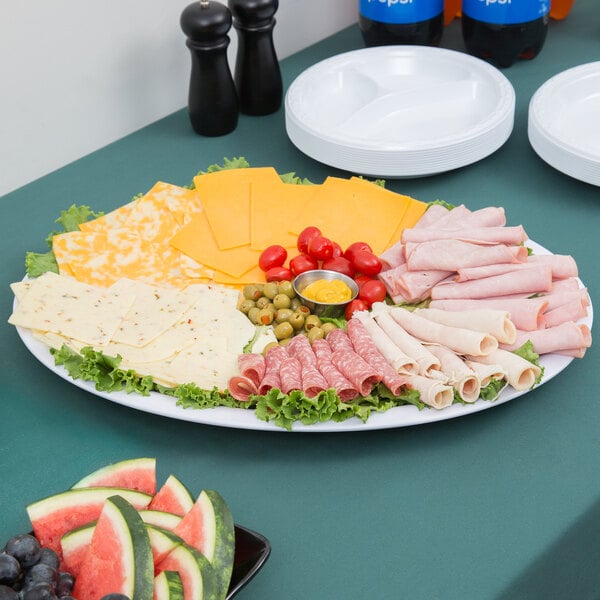 A white oval Carlisle melamine catering platter of cheese, meat, and fruit on a table.