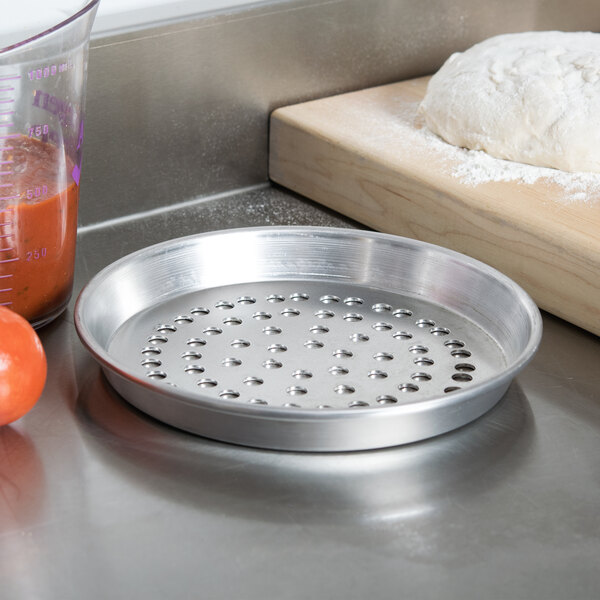 An American Metalcraft Super Perforated Deep Dish Pizza Pan with dough and tomatoes next to it.