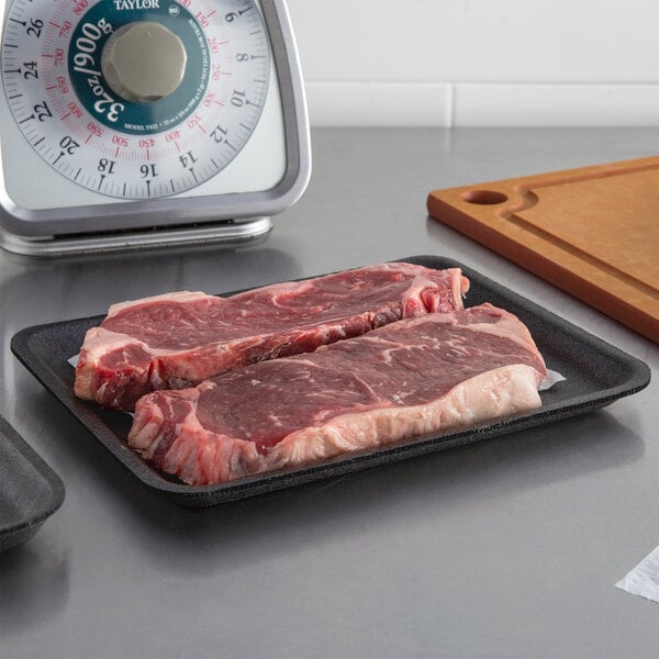 A pair of steaks on a black CKF foam meat tray on a counter.