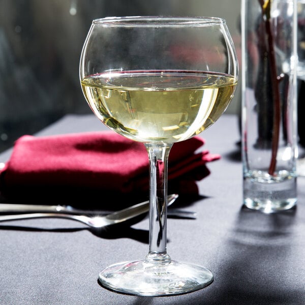 A Libbey round wine glass filled with white wine on a table.