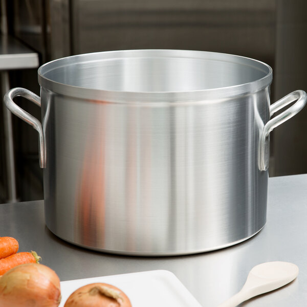 A large silver Vollrath Wear-Ever sauce pot on a counter with carrots and onions inside.
