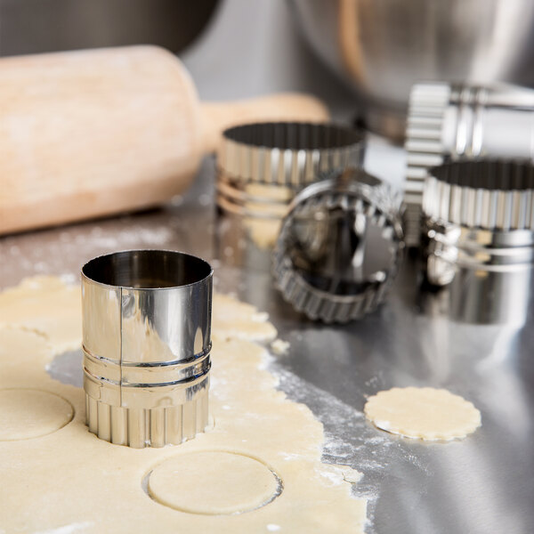 A set of Ateco round pastry cutters and a rolling pin cutting dough on a table.
