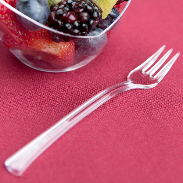 A clear plastic Fineline Tiny Tines tasting fork in a bowl of fruit.