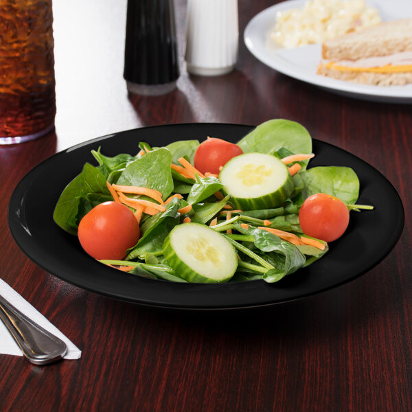 A black melamine bowl filled with a salad with tomatoes, cucumbers, carrots, and spinach.