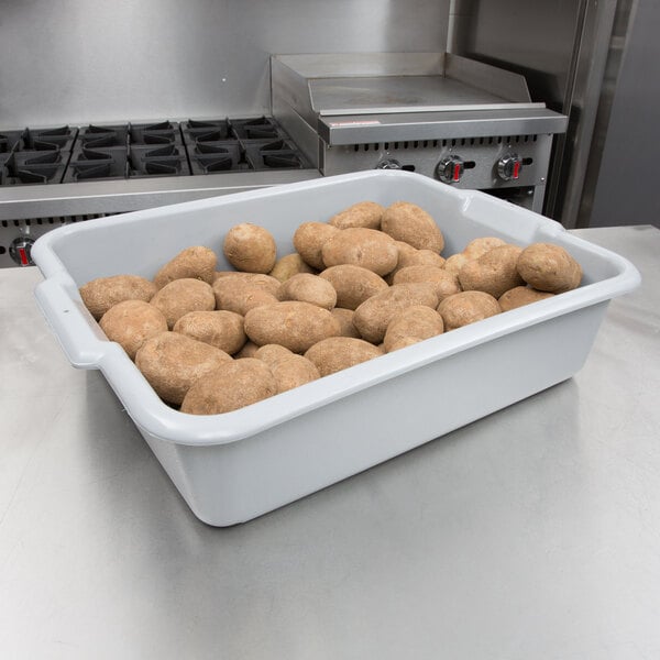A white Vollrath bus tub full of brown potatoes on a counter.