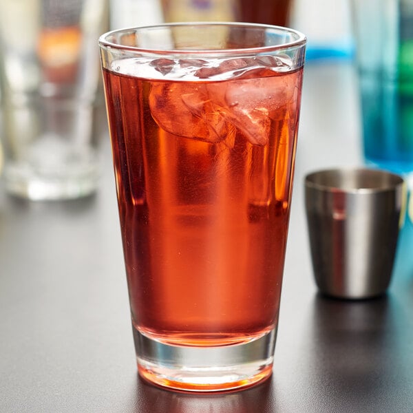 A Libbey stackable pint glass filled with red liquid and ice on a table in a cocktail bar.