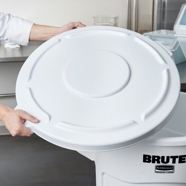 A woman holding a white lid on top of a trash can.