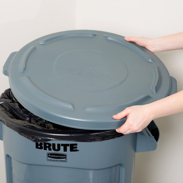 A person's hand reaching for a grey Rubbermaid trash can lid.
