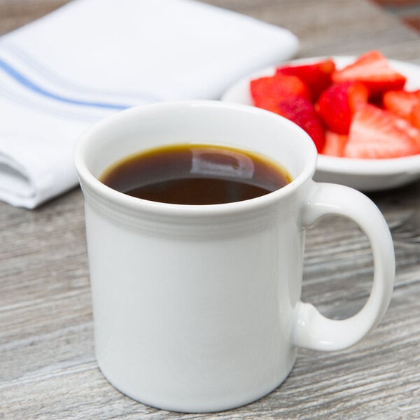 A white Fiesta Java mug filled with coffee next to a bowl of strawberries.