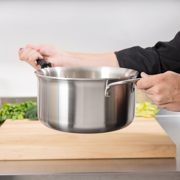 A person holding a Vollrath stainless steel sauce pan over a cutting board.