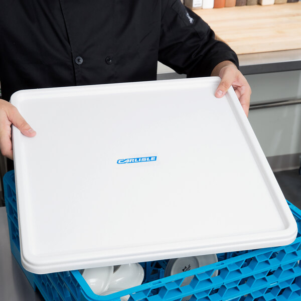 A person wearing a black coat holding a white Carlisle plastic tray.