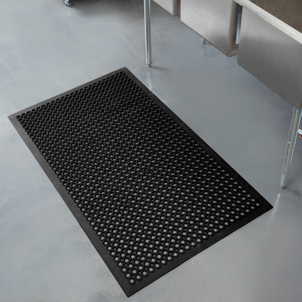 A black rubber Notrax anti-fatigue floor mat with holes in it.