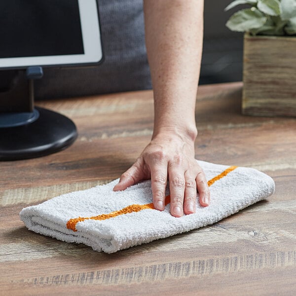 A hand using a Choice gold striped bar towel to wipe a counter.