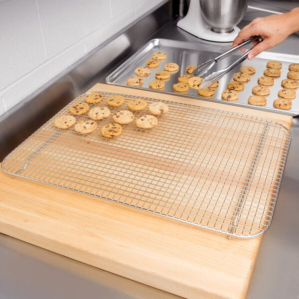A person using a Vollrath footed stainless steel cooling rack on a cookie sheet to bake cookies.