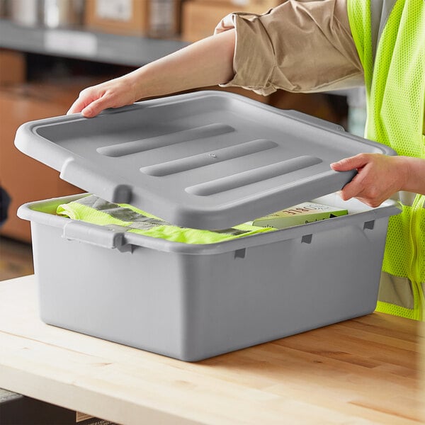 A person in a yellow vest opening a Choice gray plastic bus tub lid.