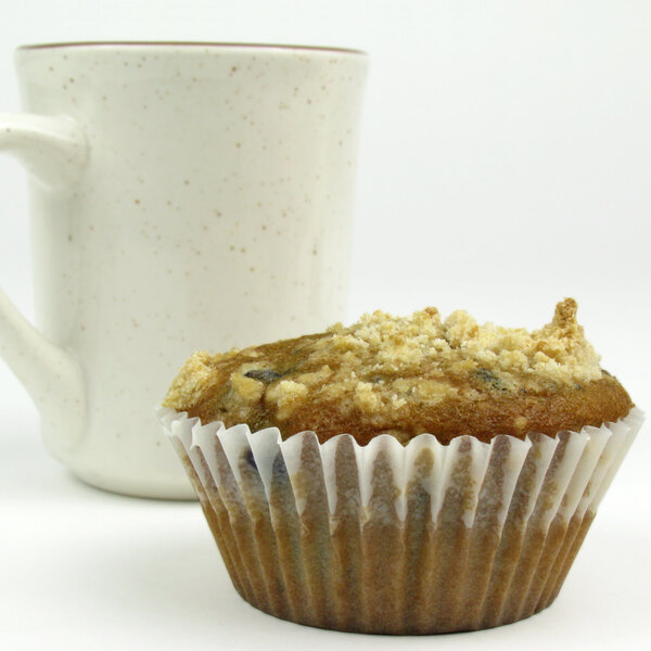 A white fluted baking cup with a muffin in it sitting next to a mug.