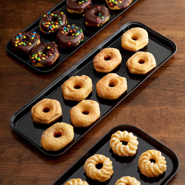 A black Cambro market tray holding chocolate donuts with candy on top.