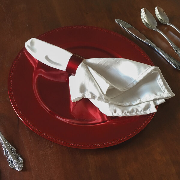 A Tabletop Classics red plastic charger plate with silverware and a napkin on a table.