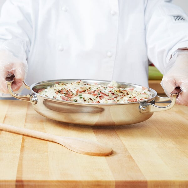 A chef holding a Vollrath Miramar oval au gratin pan of food.