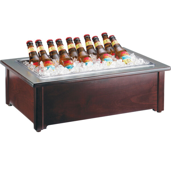 A Cal-Mil dark wood ice cooler with a clear pan full of beer bottles.