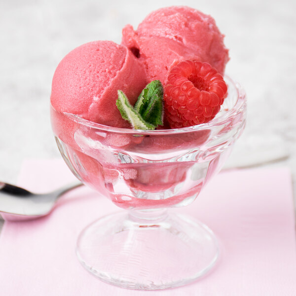 A Libbey glass cup with a scoop of ice cream with raspberries and mint.