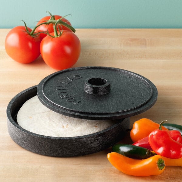 A round black container with a lid open and a tortilla inside.