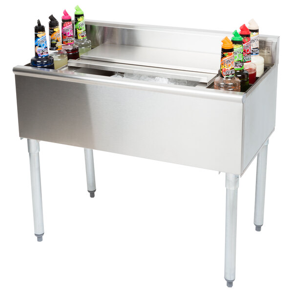 A stainless steel Eagle Group underbar cocktail and ice bin with bottles of drinks on top.