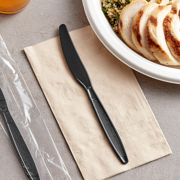 A black Visions plastic knife on a napkin next to a plate of chicken and rice.
