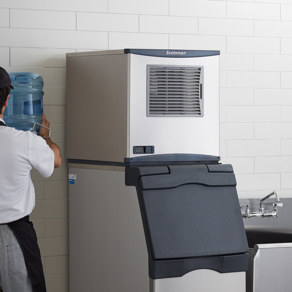 A man standing next to a black and silver Scotsman Prodigy Series air cooled ice machine.