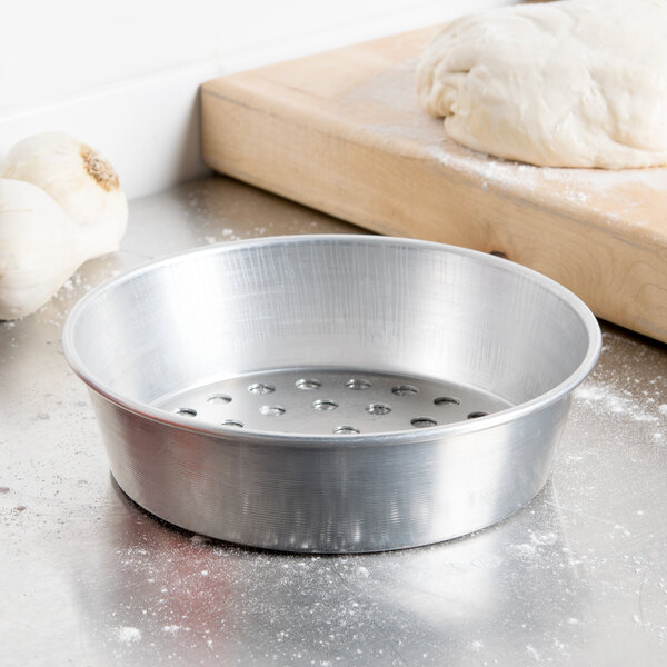 A silver American Metalcraft pizza pan with holes in it filled with dough.