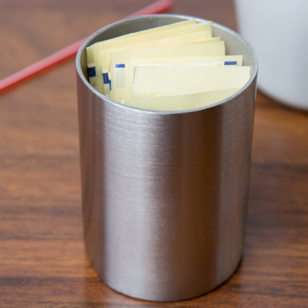 A silver Tablecraft stainless steel sugar caddy with yellow papers inside.