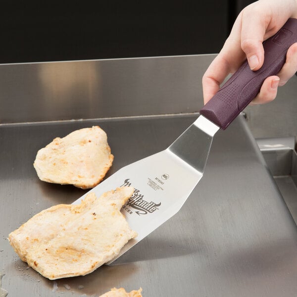 A hand using a Mercer Culinary Hell's Handle spatula to turn food on a grill.