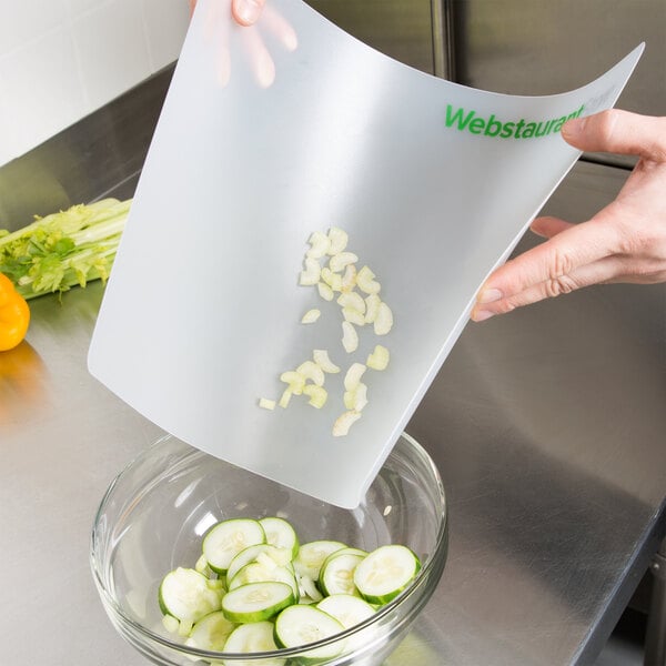 A person using a WebstaurantStore flexible cutting board to chop cucumbers.