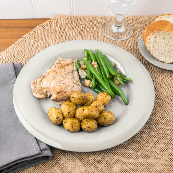 A Carlisle Sierrus melamine plate with chicken, potatoes and green beans, a plate of bread, and a glass of wine.