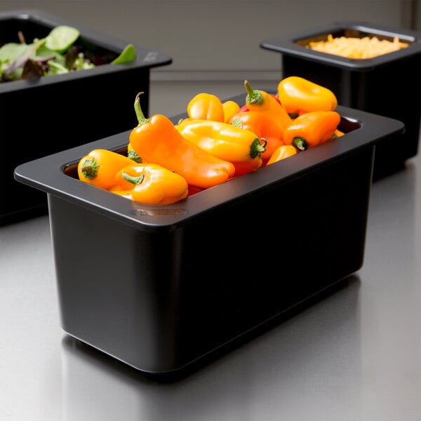 A Cambro black 1/3 size food pan filled with orange peppers on a counter in a salad bar.
