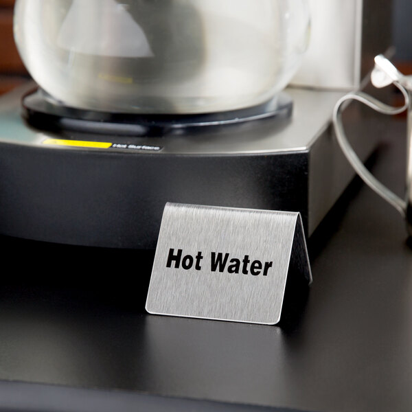 A Tablecraft stainless steel "Hot Water" tent sign on a hot water dispenser.