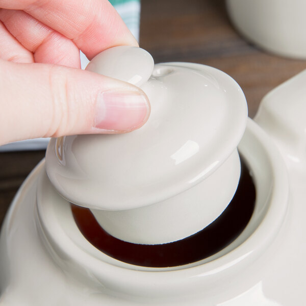 A hand holding a white Hall China teapot lid.