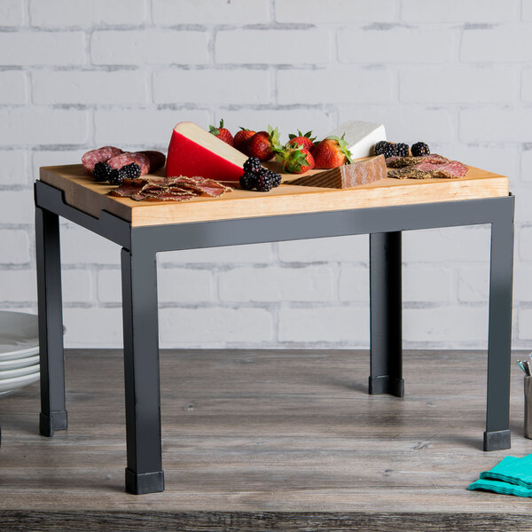 A Tablecraft butcher block riser with fruit and meat on it displayed on a table with food.