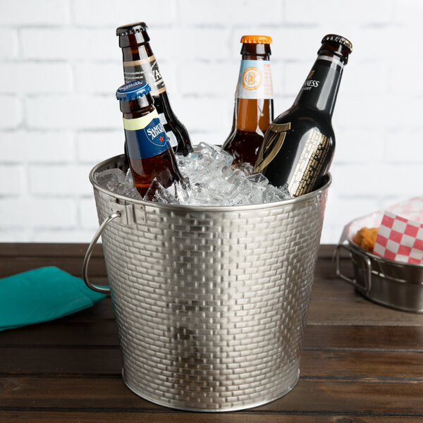 A Tablecraft stainless steel beverage pail filled with ice and beer bottles on a table.