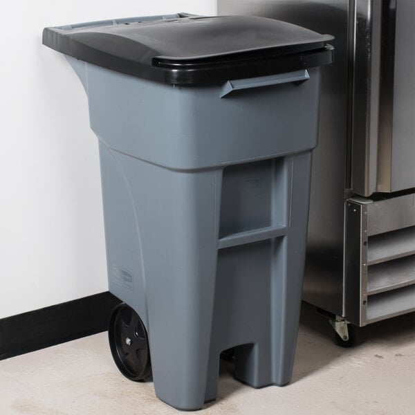 A Rubbermaid grey rectangular trash can with a black lid and wheels.