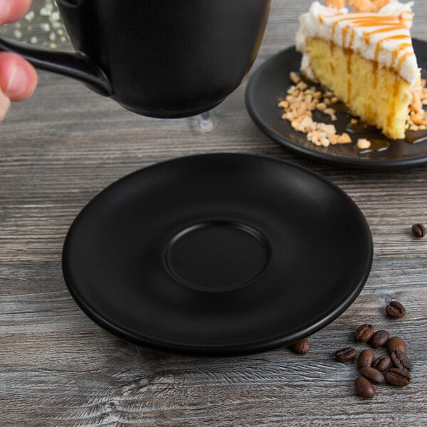 A Libbey Driftstone Onyx Satin Matte porcelain saucer under a black mug holding a cup of coffee over a plate of cake.
