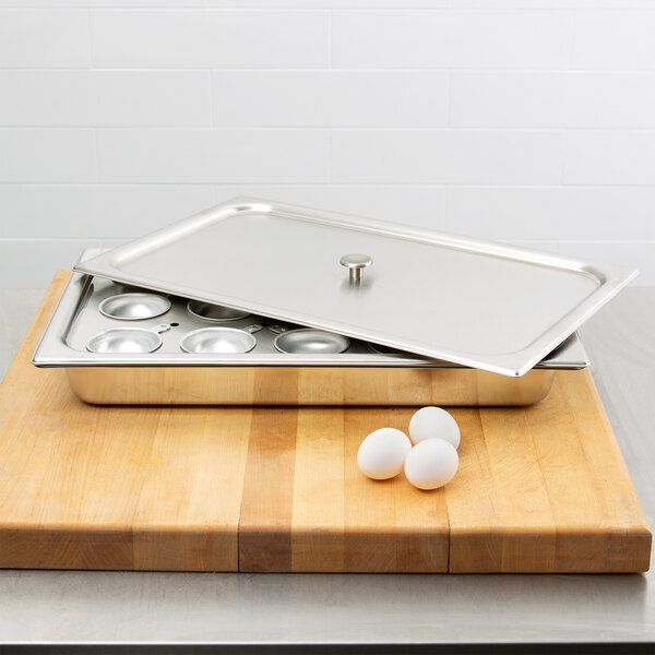 A Vollrath stainless steel egg poacher tray with eggs and a lid open.