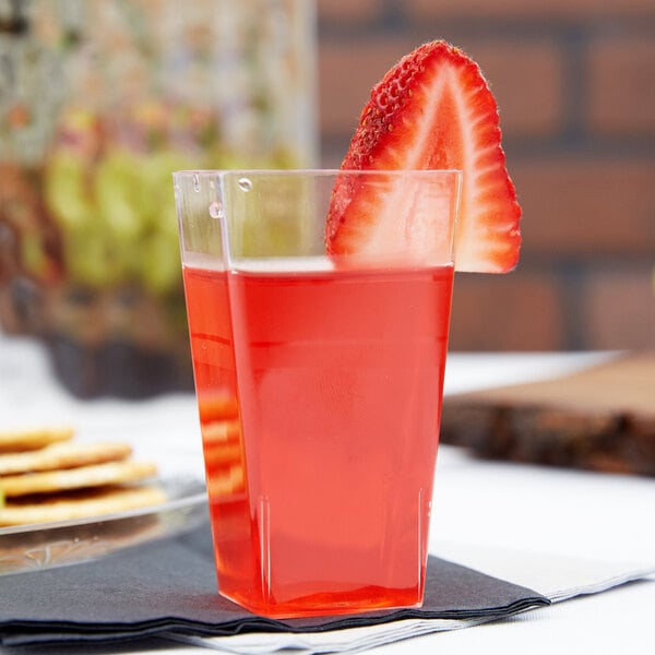 A clear Fineline Tiny Tumbler filled with red liquid and a straw, with a strawberry on the rim.